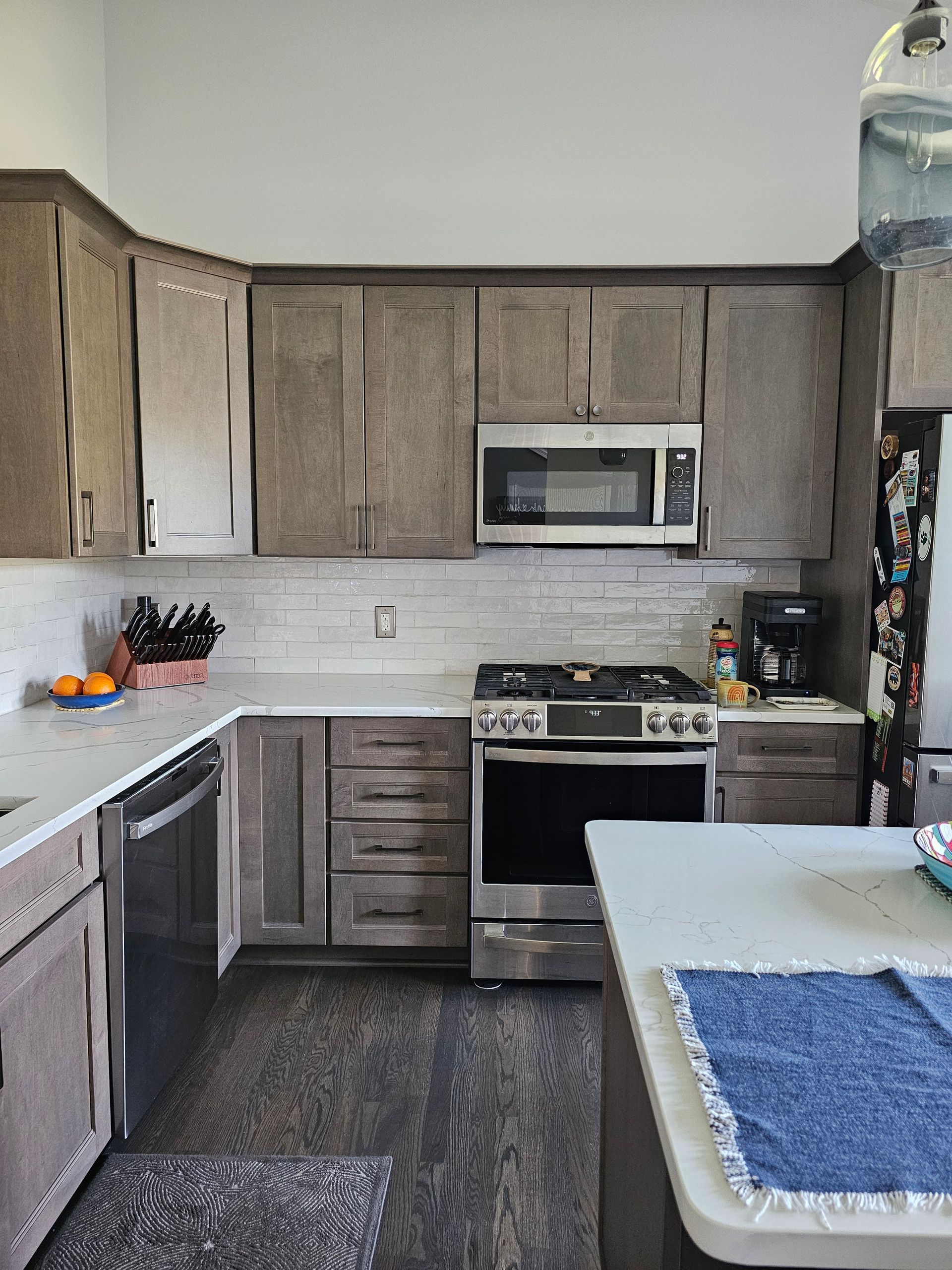 Kitchen with gray cabinets, stainless steel appliances, white countertops, and dark wood-look flooring.