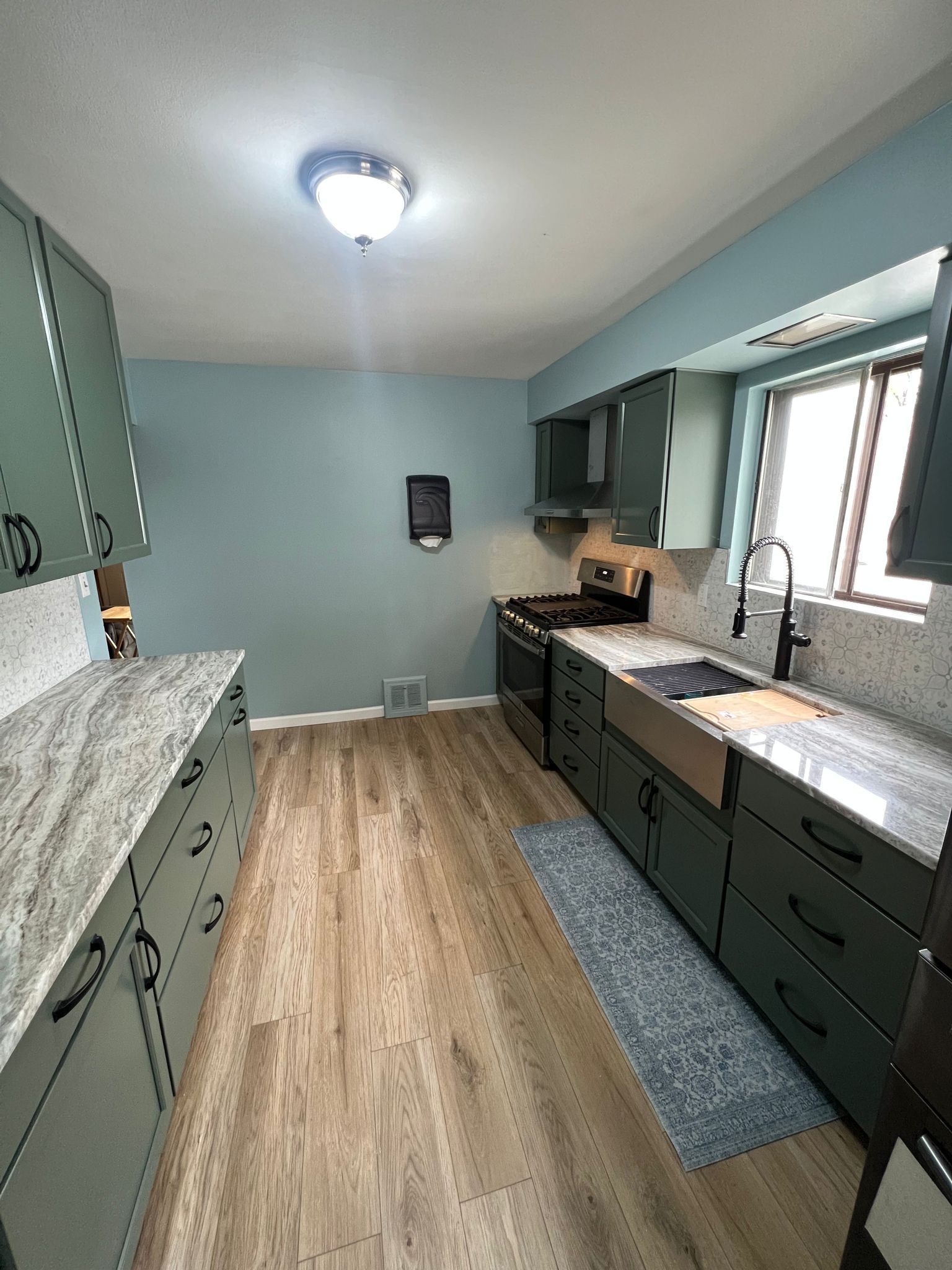 Green kitchen cabinets and countertops, blue walls, wooden floor.