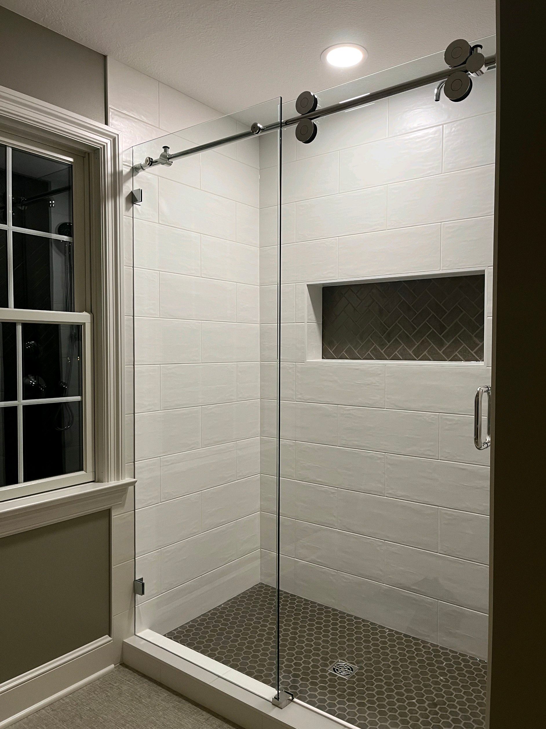 Modern bathroom with glass shower door, light tile, dark floor, and inset shelf.