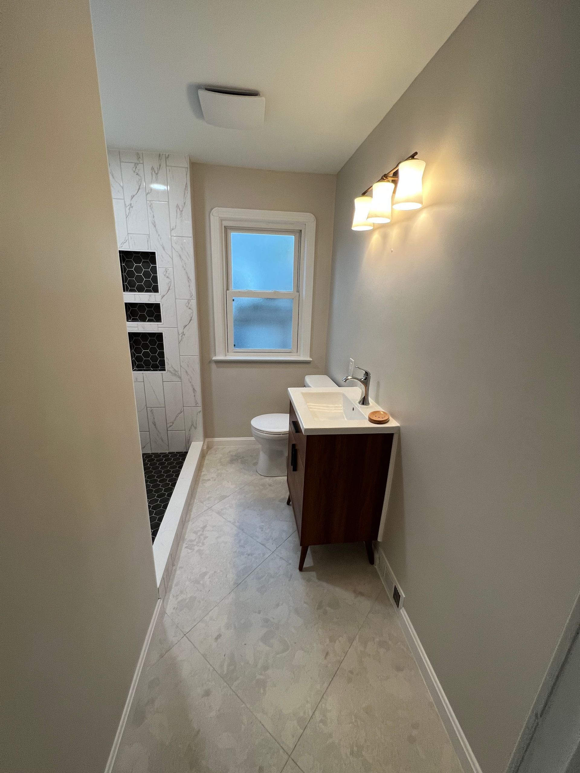 Bathroom with gray walls, vanity, toilet, window, and shower with black and white tile.
