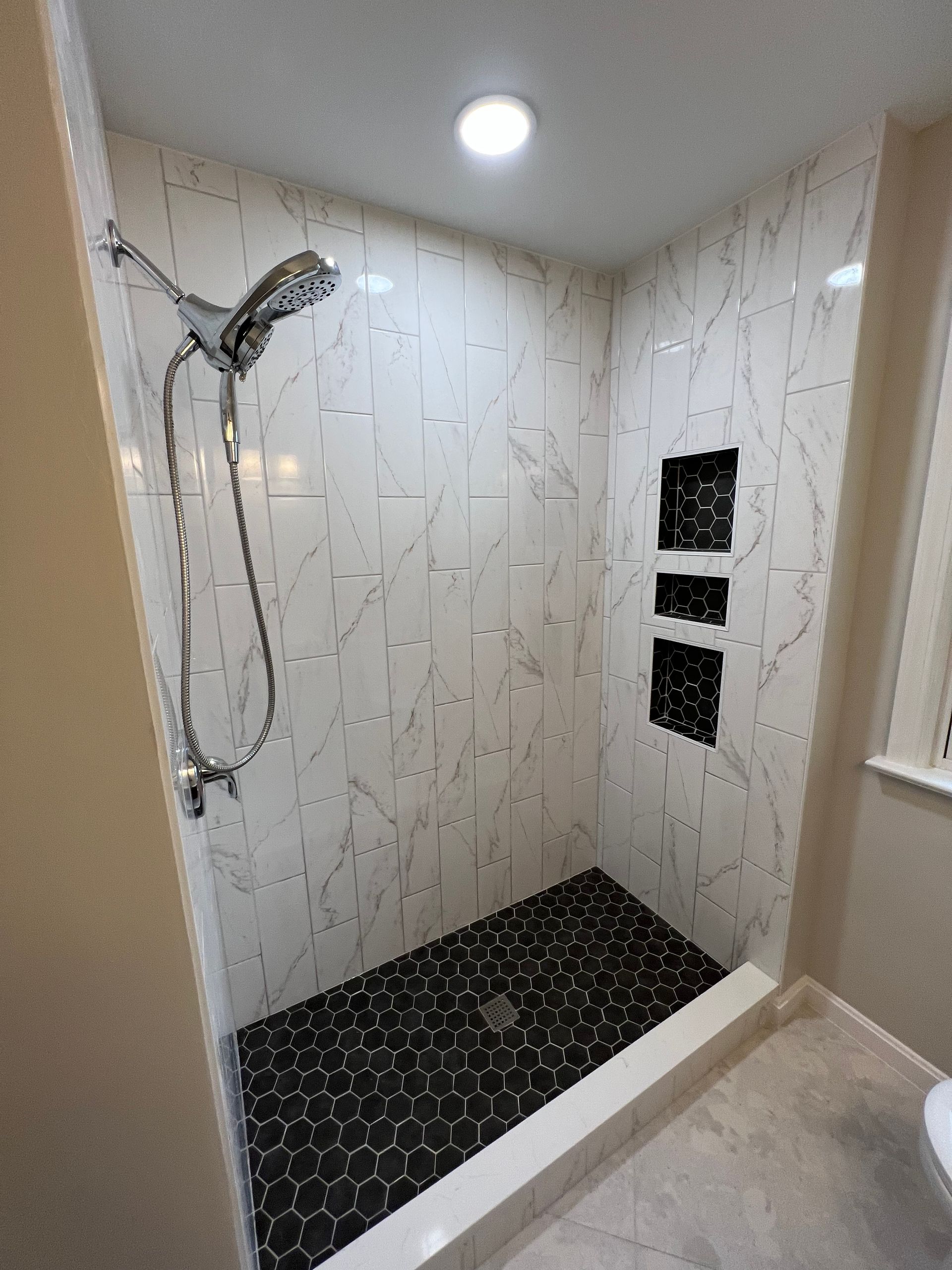 Newly tiled shower with black pebble floor, white walls, built-in shelves, and a silver showerhead.