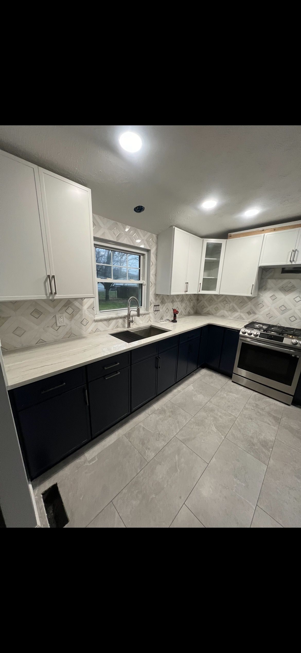 Newly remodeled kitchen with white cabinets, dark blue cabinets, and stainless steel appliances.