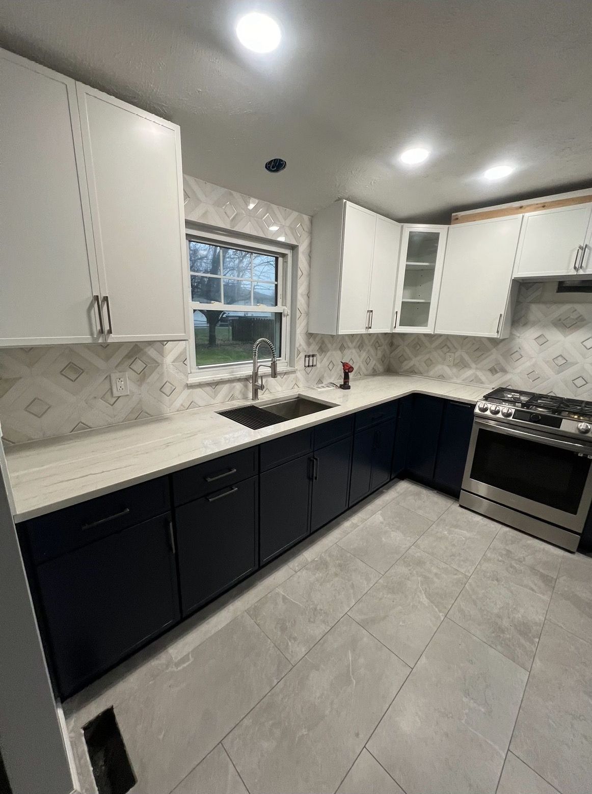 Modern kitchen with white and navy blue cabinets, light countertops, and a stainless steel stove.