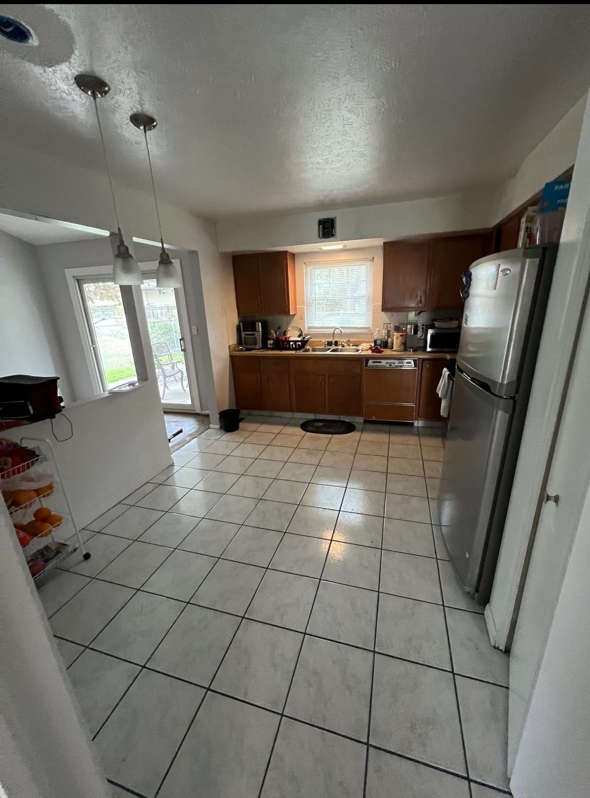 Kitchen with brown cabinets, stainless steel refrigerator, white tile floor, and a sliding glass door.