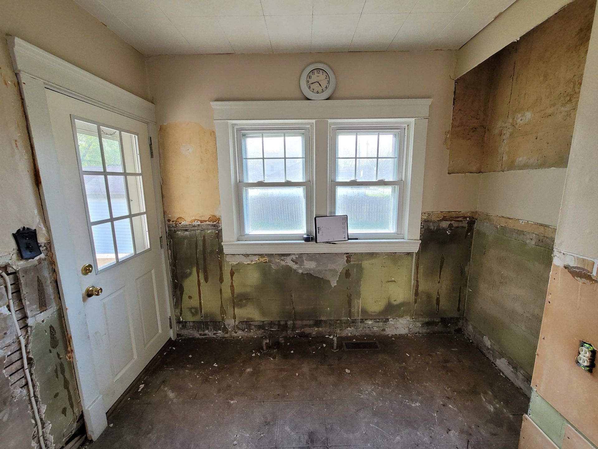 Interior room with exposed wall. A door and window are present, along with a clock.