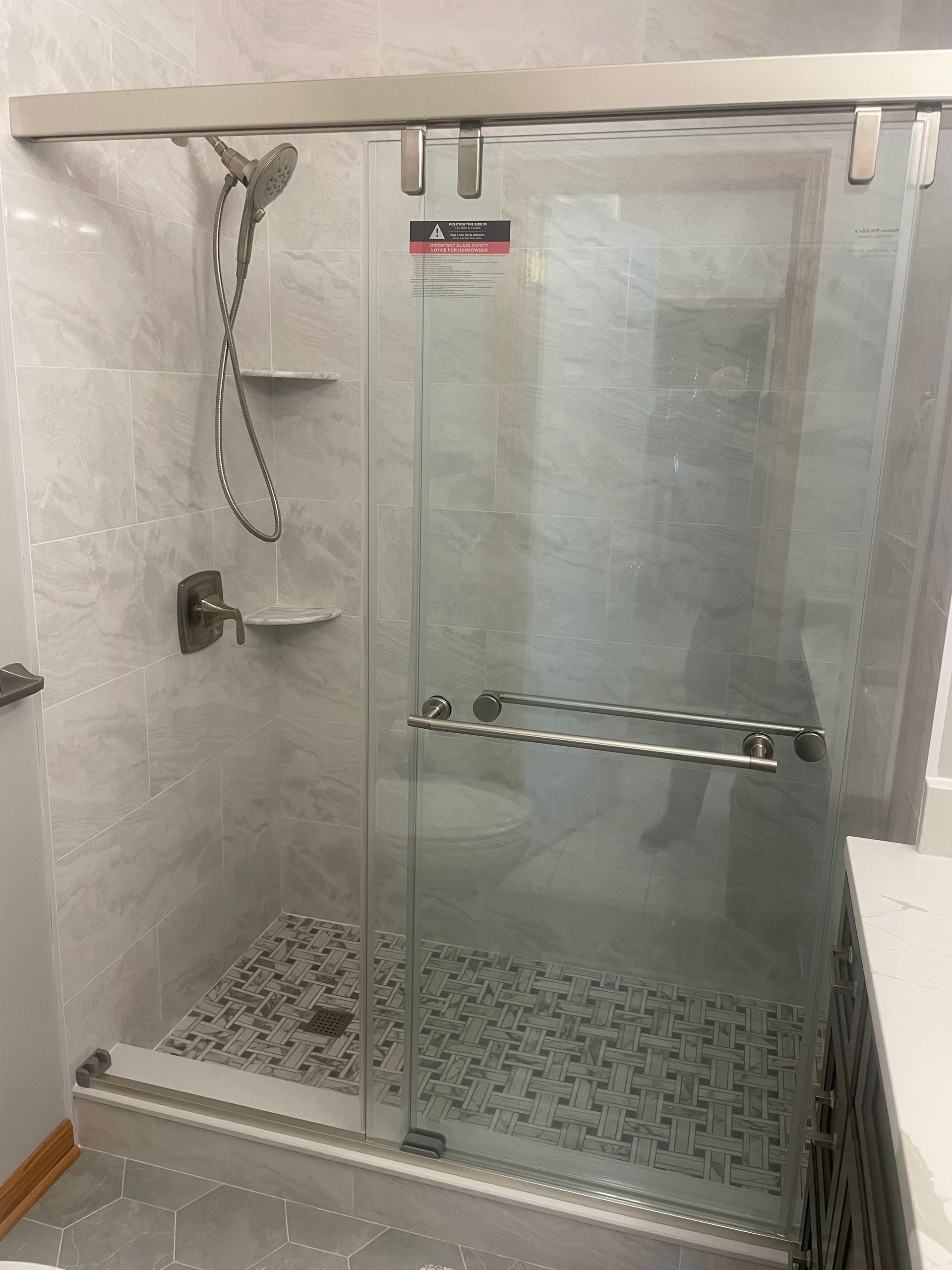 Glass shower enclosure with gray tile walls and pebble floor. Silver hardware, showerhead.