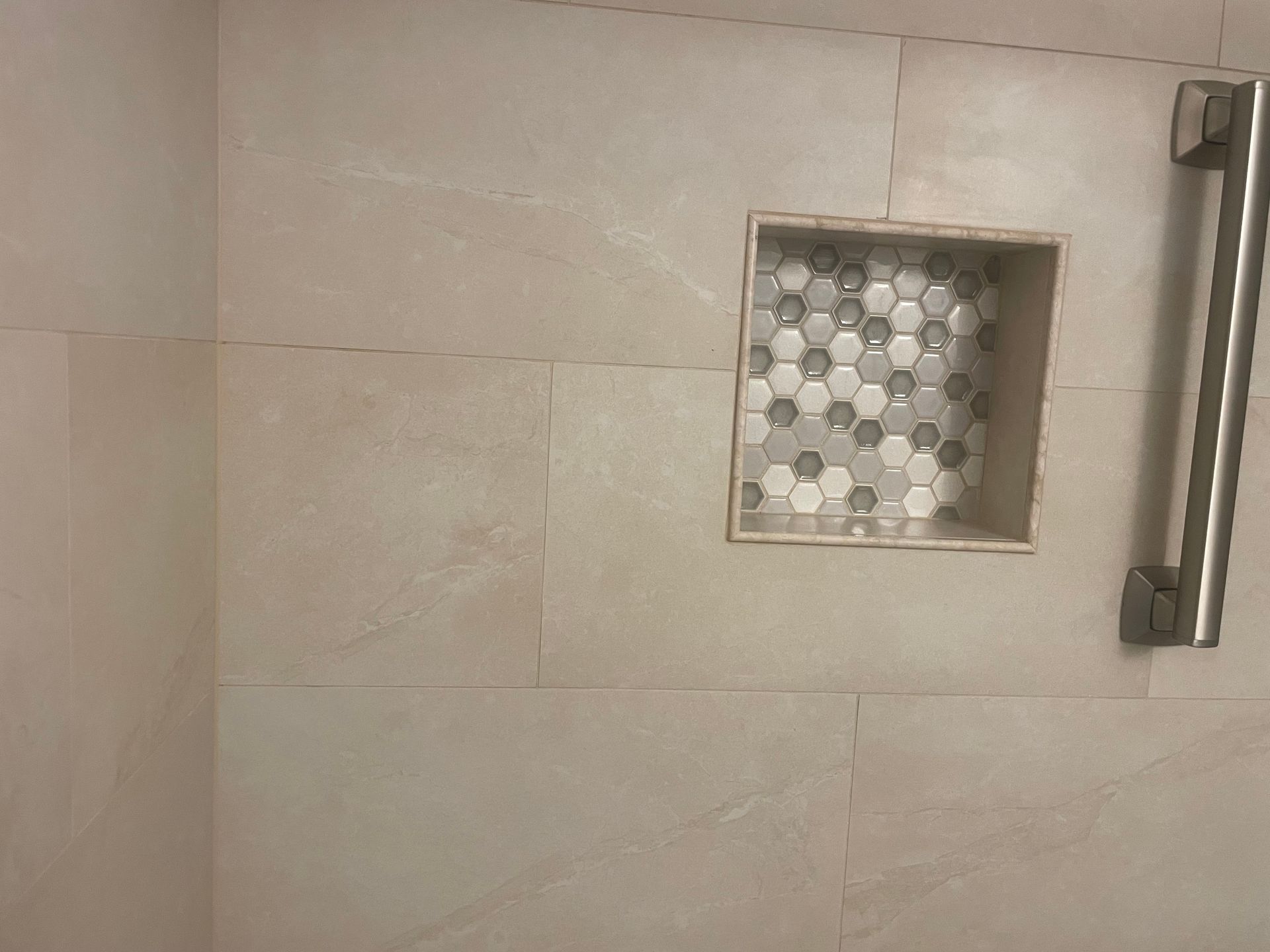 Shower with beige tile, built-in hexagon tile niche, and a stainless steel grab bar.