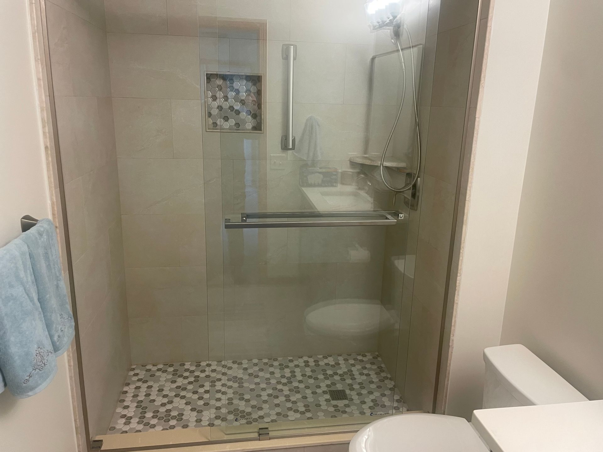 Shower with glass doors and pebble floor, beside a toilet. Light blue towel on a nearby wall.