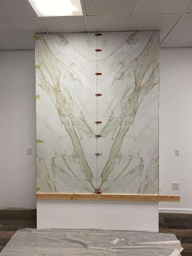 Large marble slab installation on a white wall, supported by wood, with brown veining.