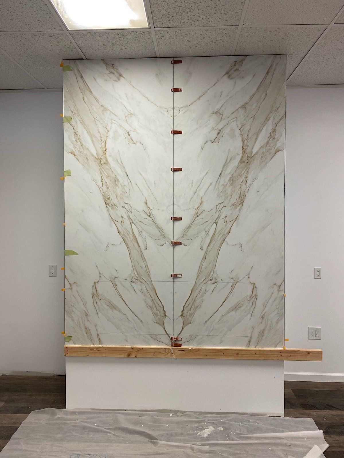 Large stone slab against a white wall, with copper clips and a wooden support.