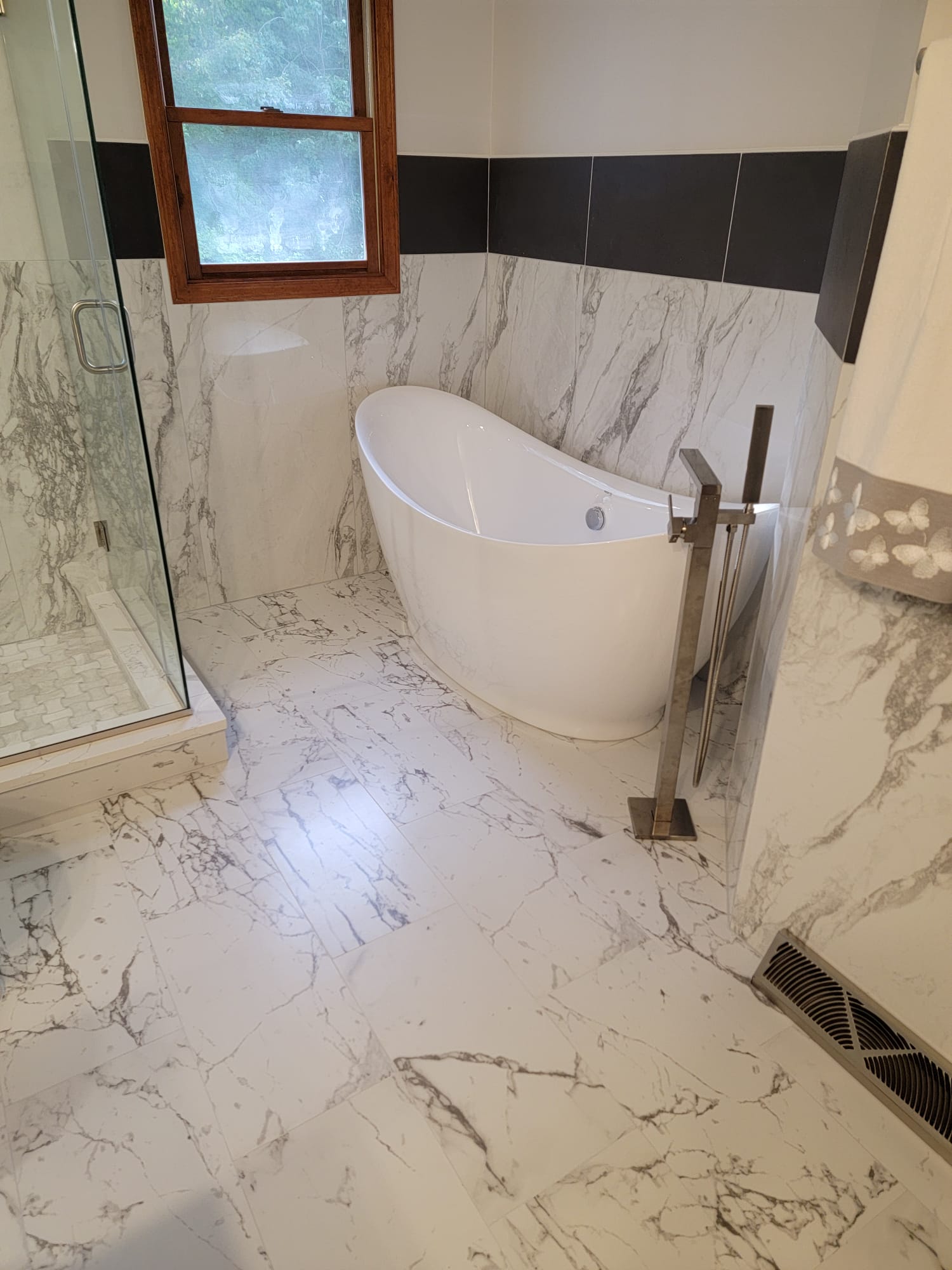 Bathroom with white marble tile, a freestanding bathtub, and a glass shower.