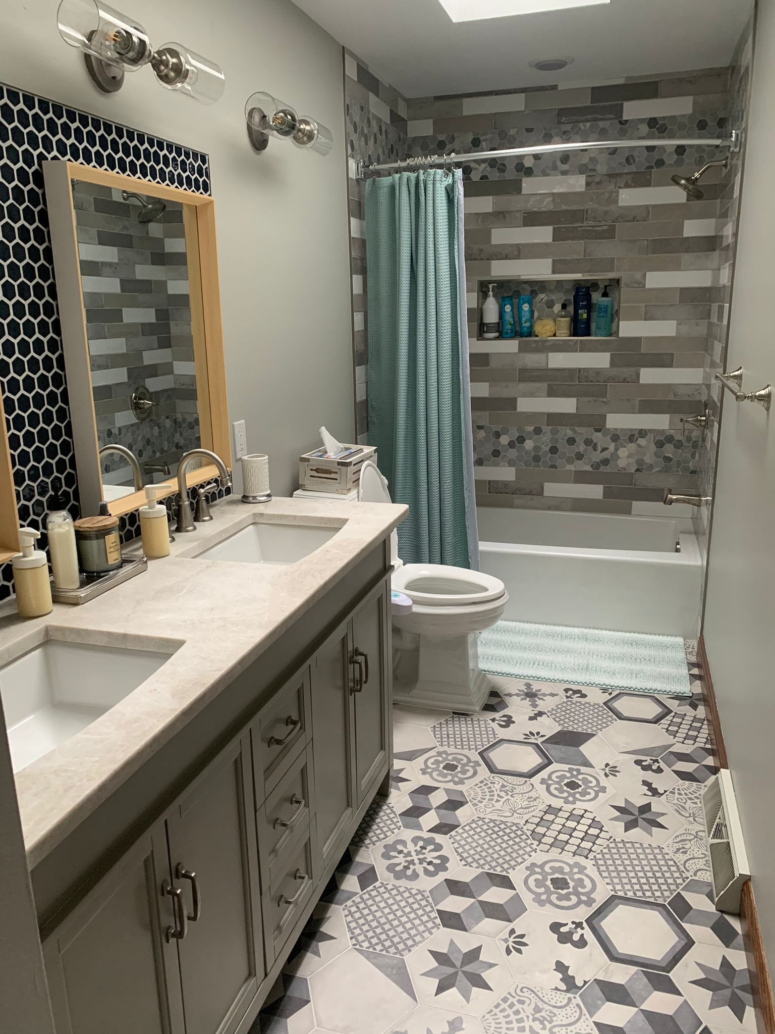 Bathroom with double vanity, patterned floor tiles, and a bathtub with a tiled accent wall.