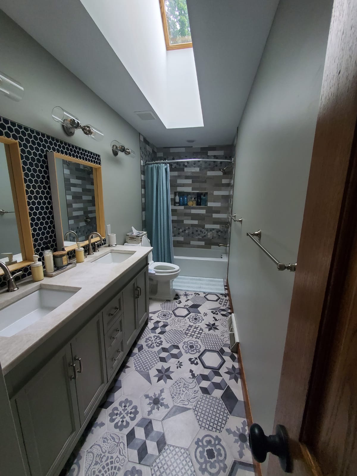 Bathroom with gray walls, patterned floor, double vanity, and a skylight.