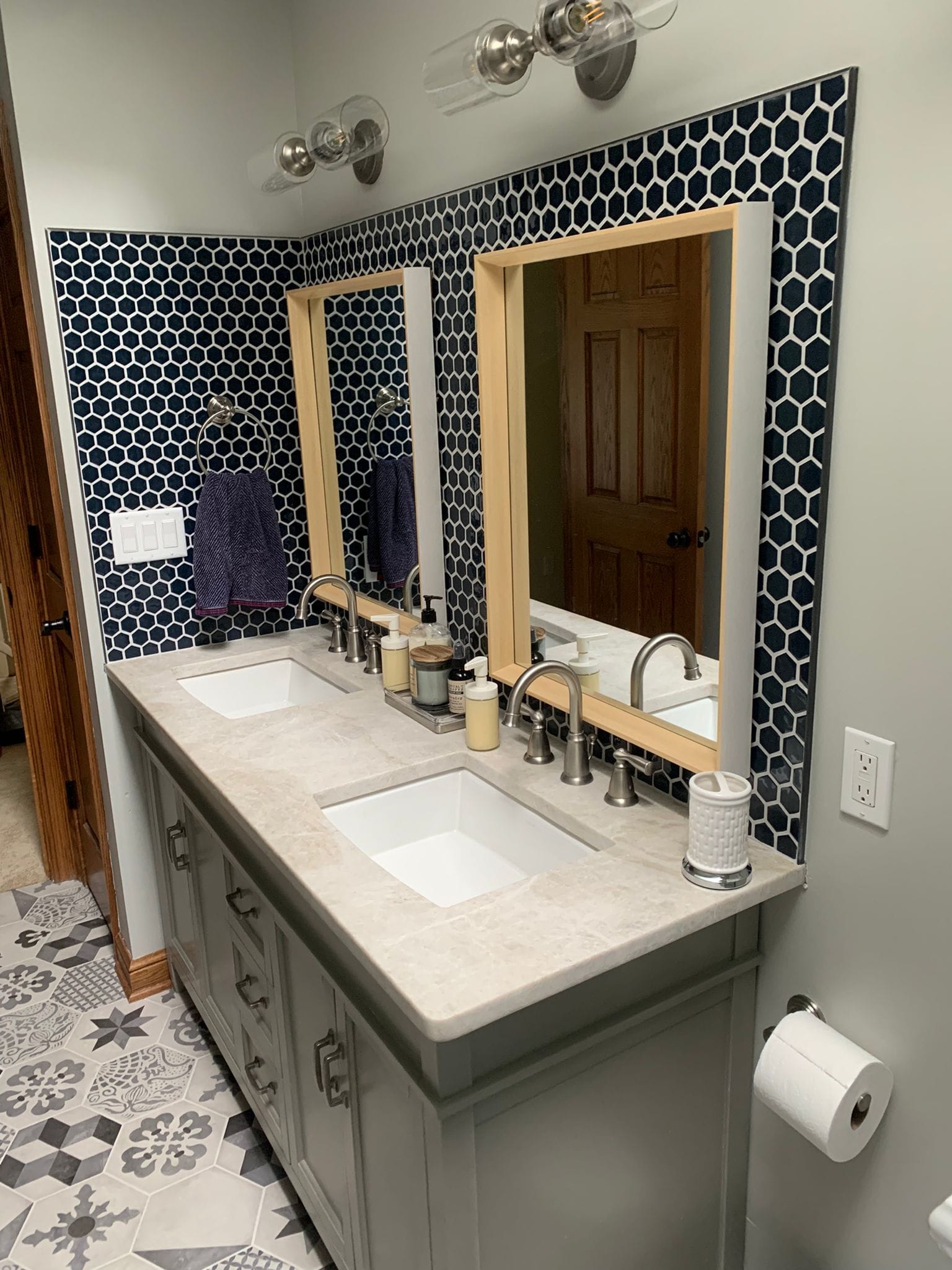 Bathroom with gray vanity, double sinks, patterned tile backsplash, and wood-framed mirrors.