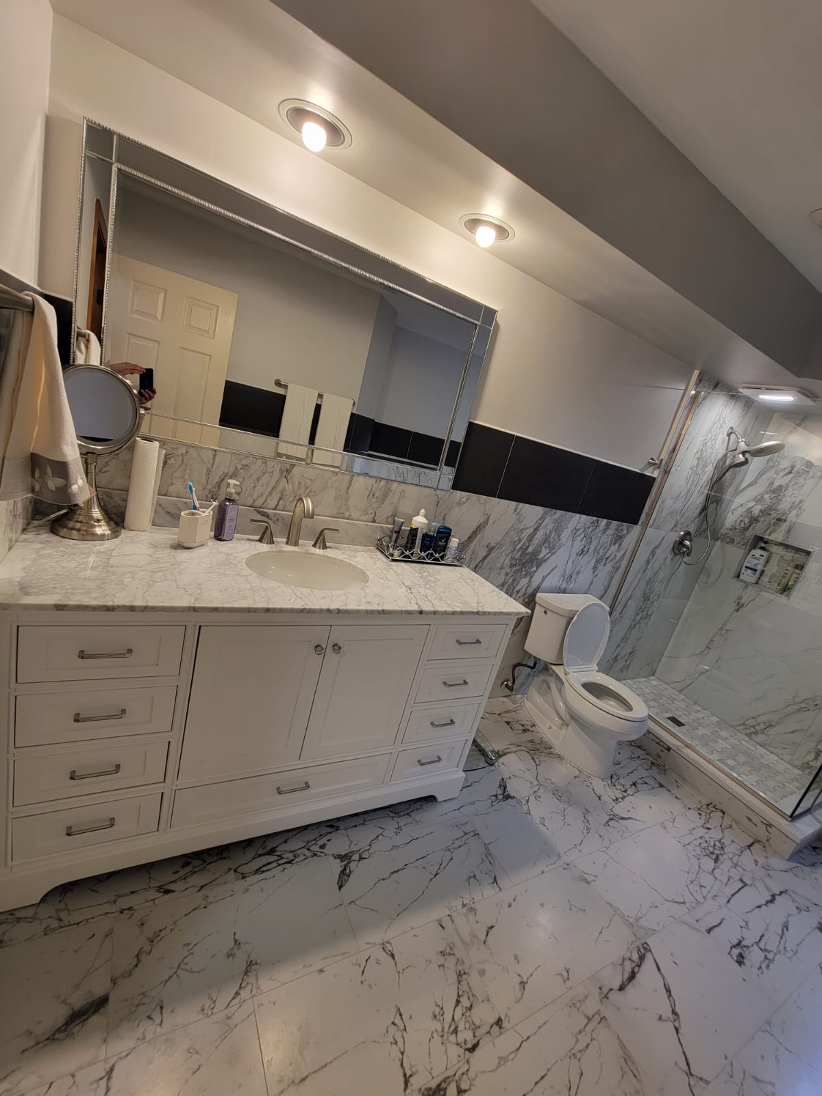 White marble bathroom with white vanity, large mirror, and glass shower.
