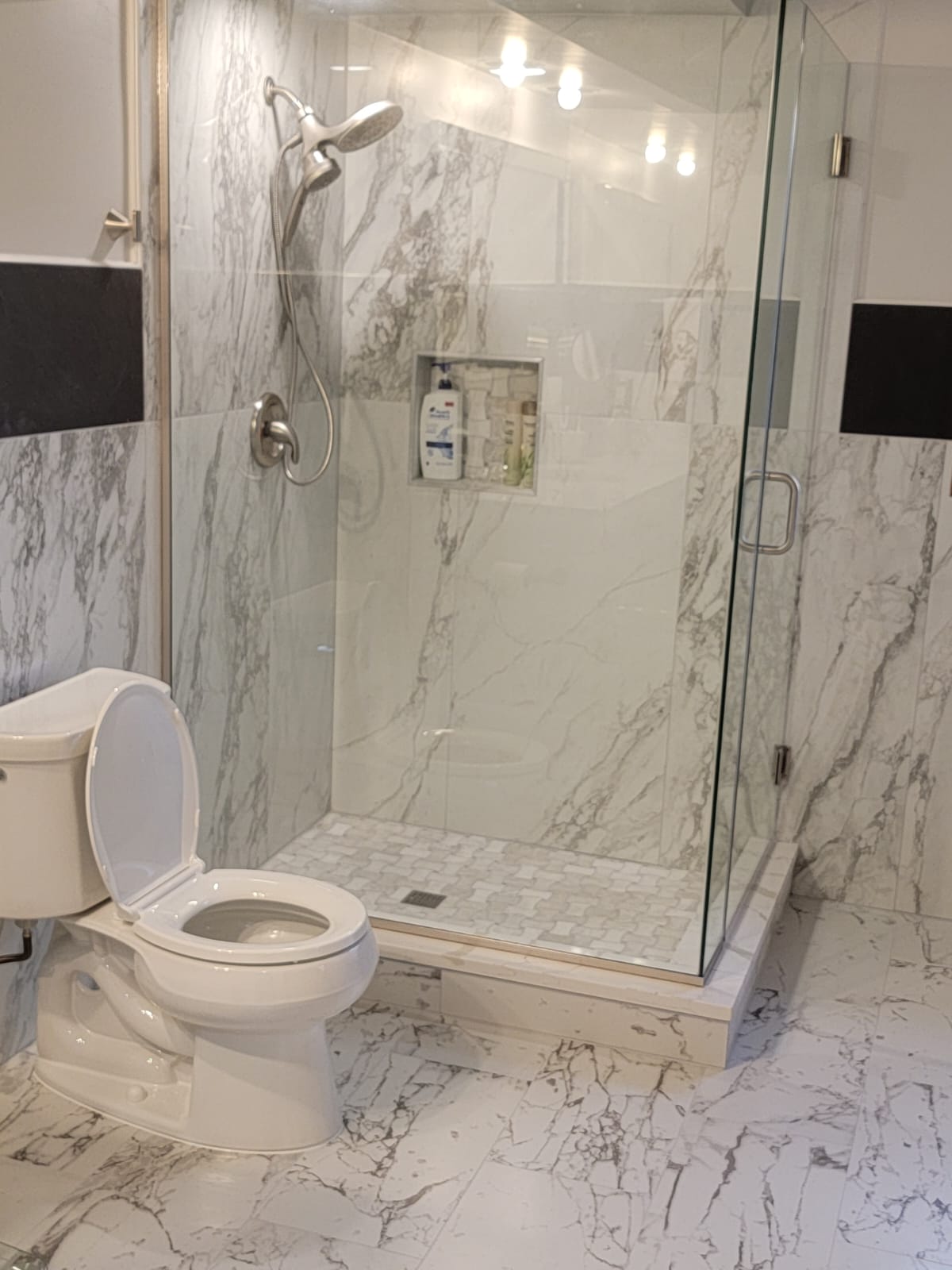 Modern bathroom with a glass shower, marble-patterned walls and floor, and a toilet.