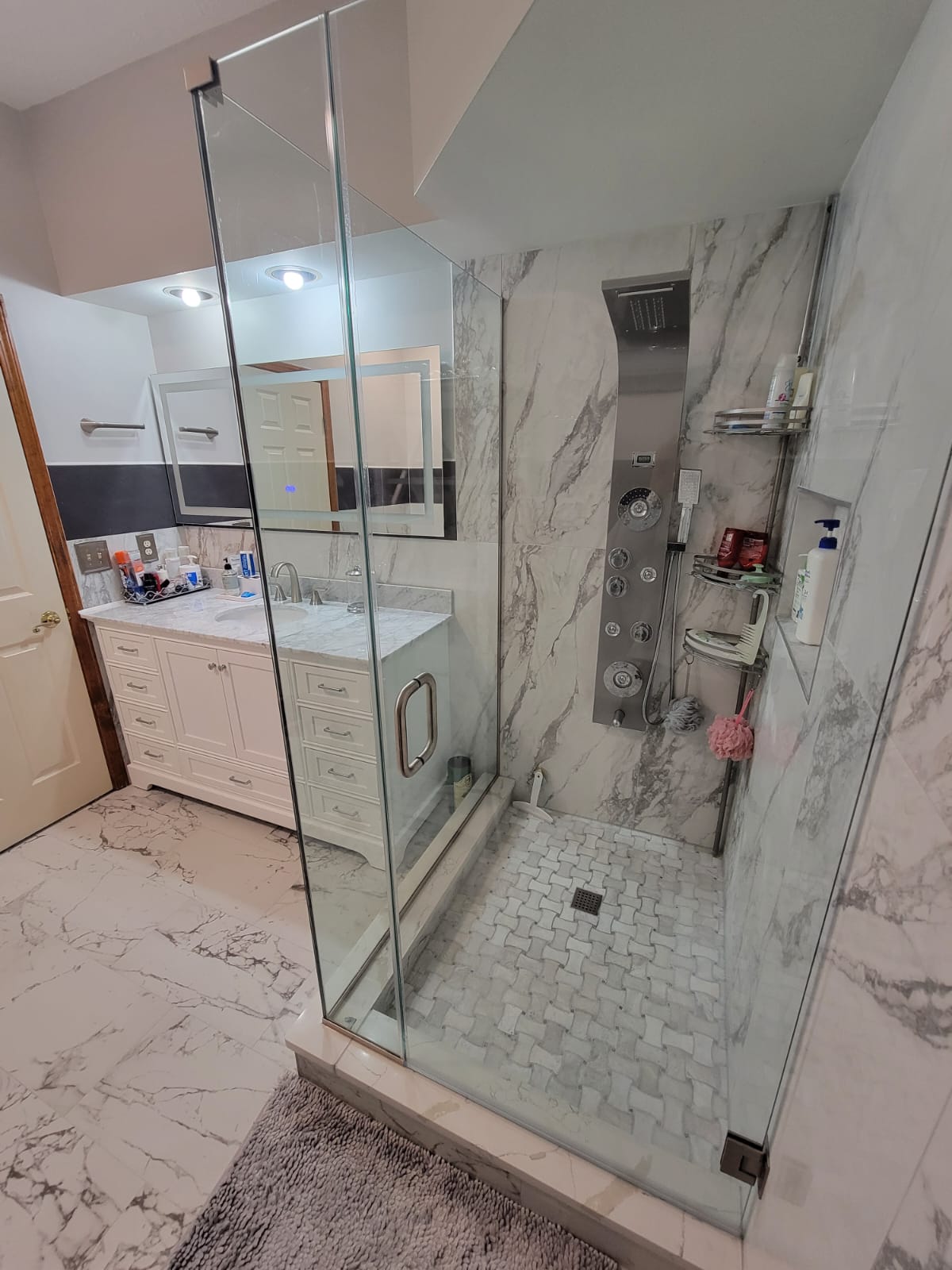 Modern bathroom with glass shower, marble walls, and white vanity.