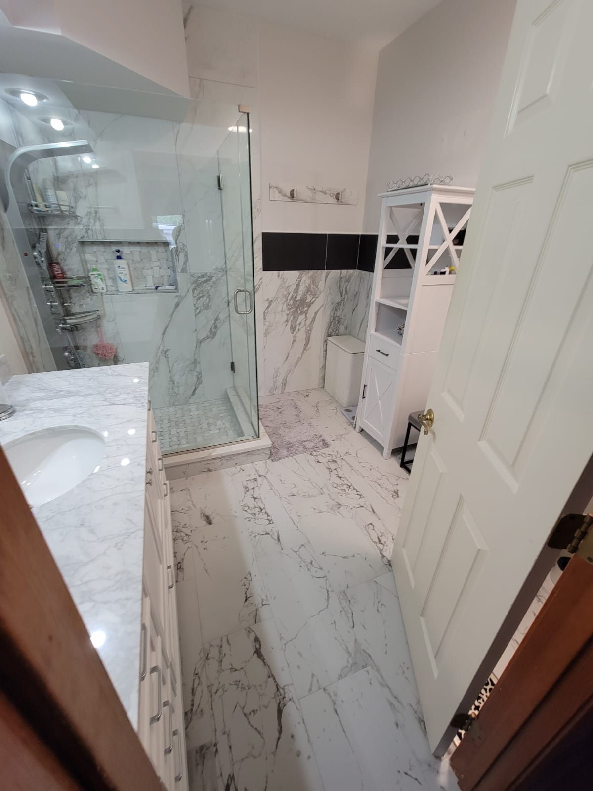 Bathroom with marble tile, glass shower, white cabinet, and open white door.