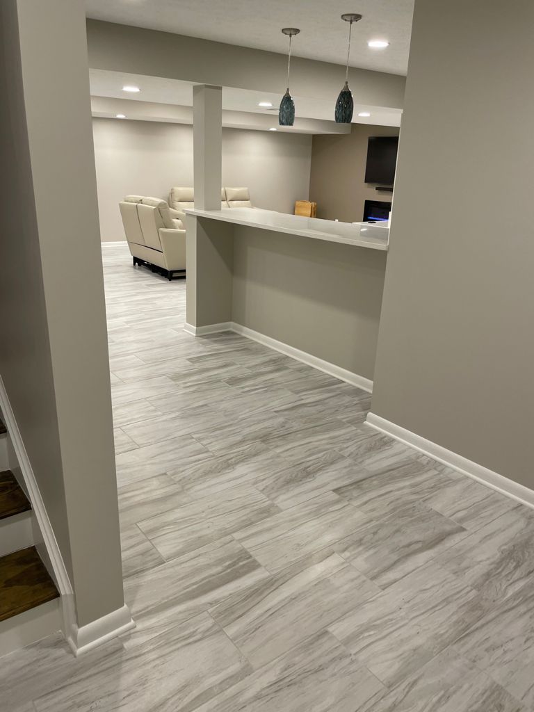 Basement interior with gray flooring, bar area, seating, and overhead lights.
