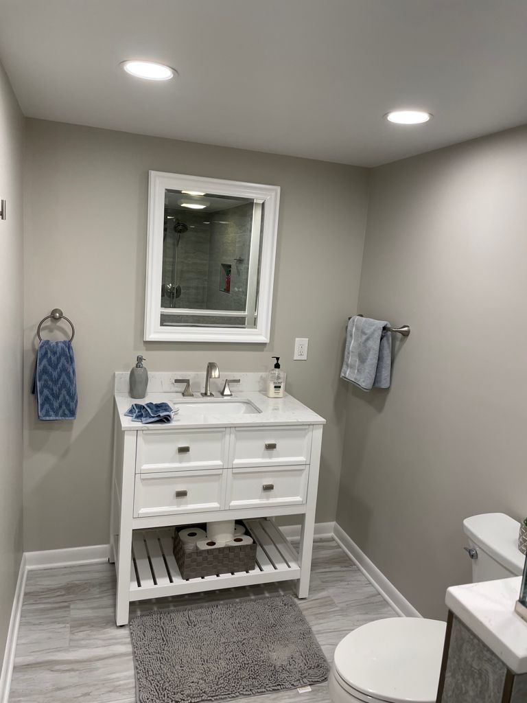 Bathroom with white vanity, gray walls, mirror, towels, and toilet.