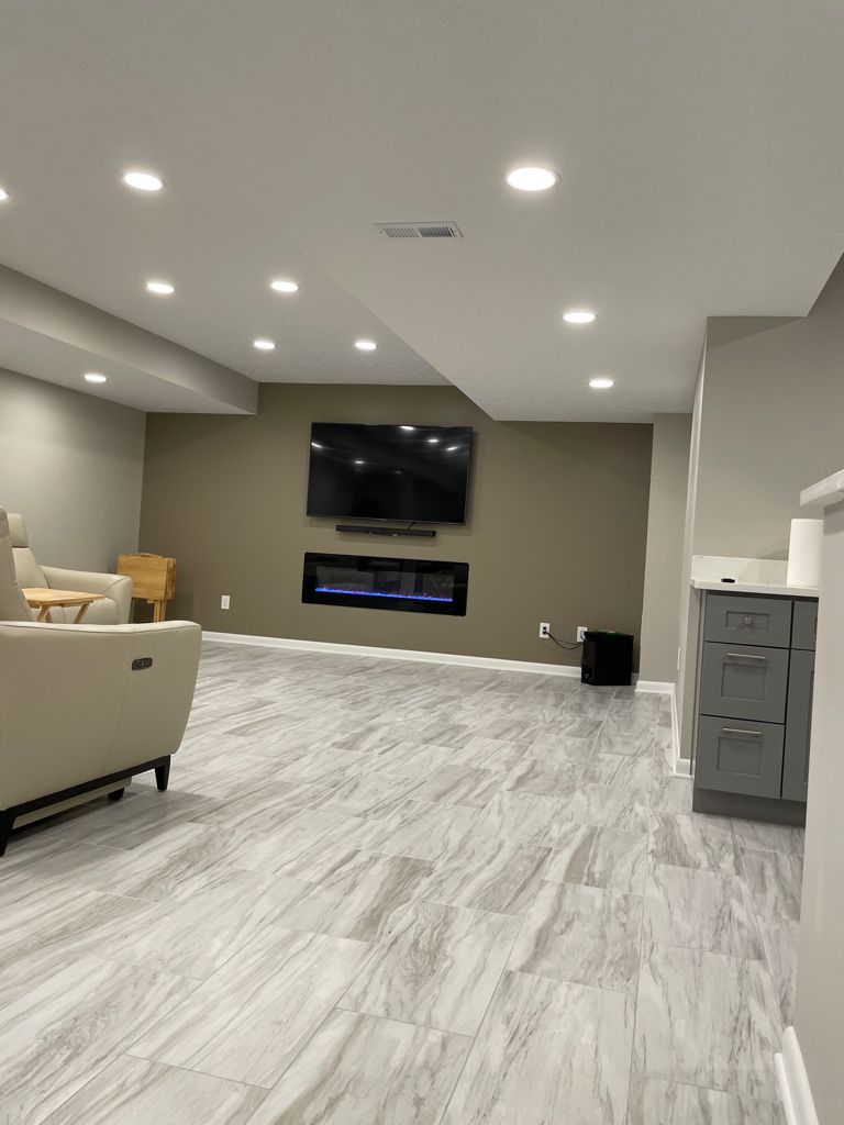 Modern living room with a TV over a fireplace, beige walls, and light gray flooring.