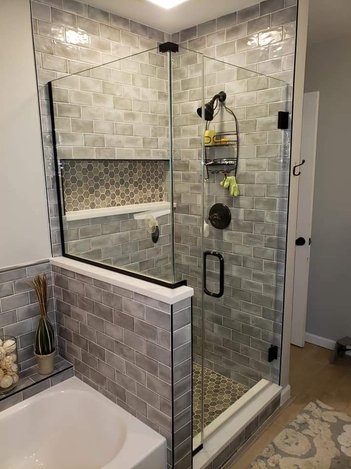A modern bathroom with a glass-enclosed shower, gray tile walls, and a built-in shelf.