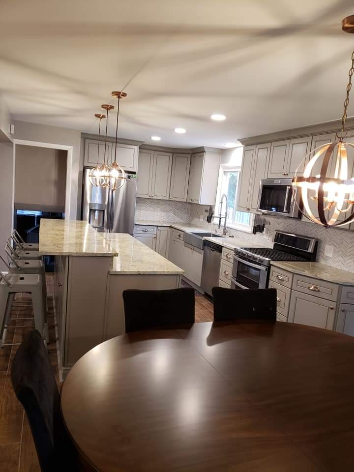 Gray kitchen with light-colored countertops, stainless steel appliances, pendant lights, and a round wooden table.