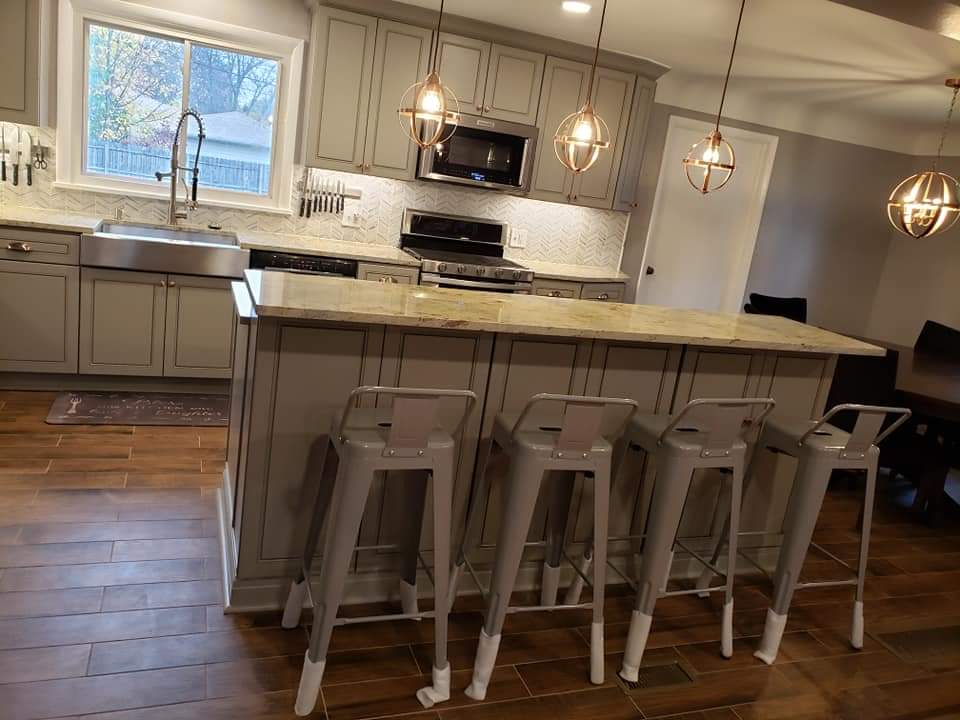 Kitchen with grey cabinets, granite countertops, island with bar stools, and pendant lights.