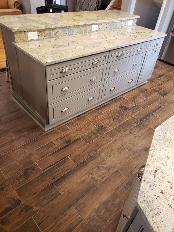 Gray kitchen island with granite countertops and wood-look tile flooring.