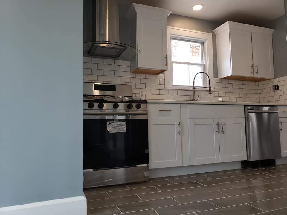 Modern kitchen with white cabinets, stainless steel appliances, and gray tiled floor.