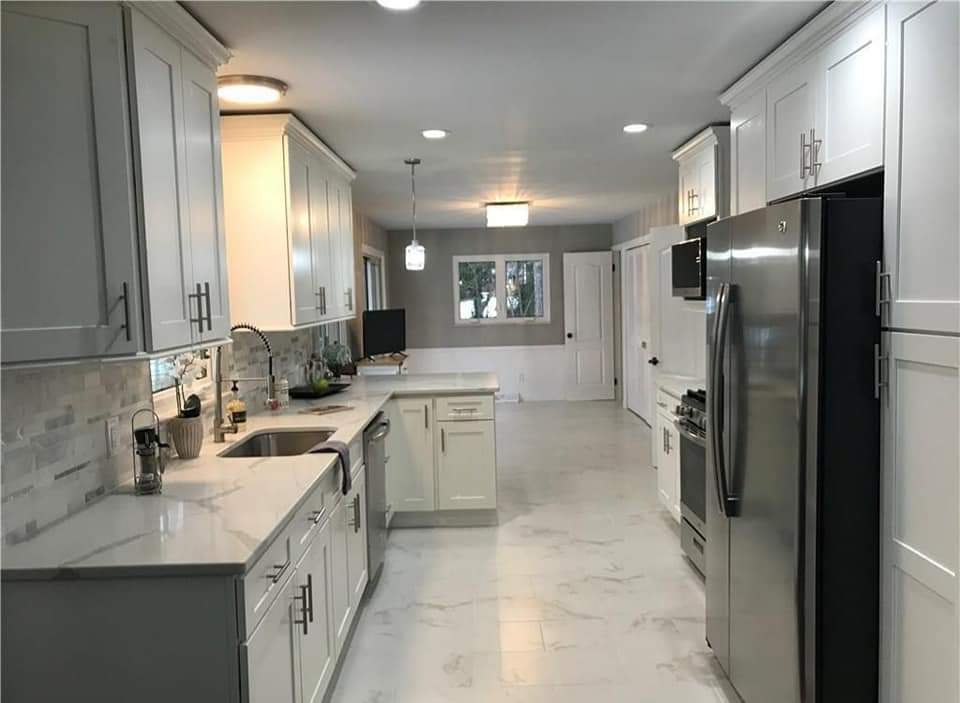 White kitchen with cabinets, marble countertops, stainless steel appliances, and a window.