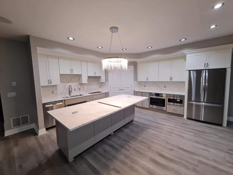 Modern kitchen with white cabinets, gray island, stainless steel appliances, and wood-look flooring.