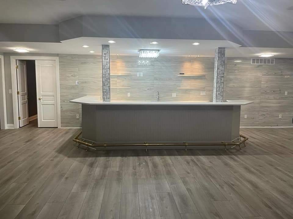 Finished basement with a bar; gray wood-look floors, white bar, decorative columns, and chandelier.