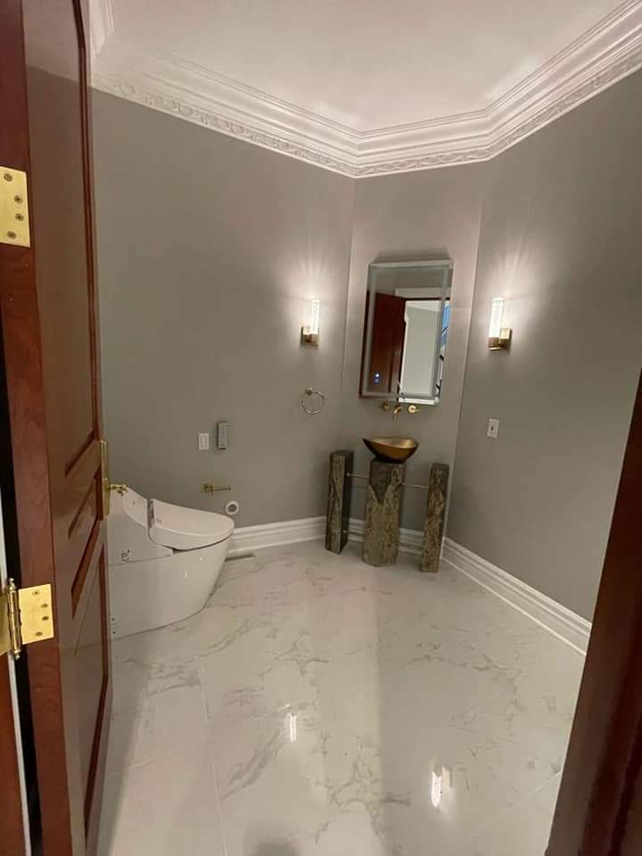 A luxury powder room with white marble floor, a modern toilet, and a decorative sink.