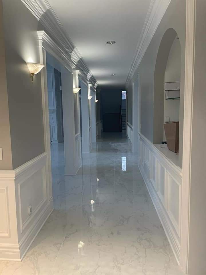 Long hallway with white molding, sconces, and polished white floor.