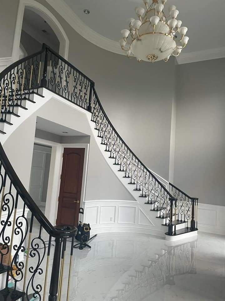 Elegant curved staircase with black and gold railing, leading to a second floor. Large chandelier hangs above.