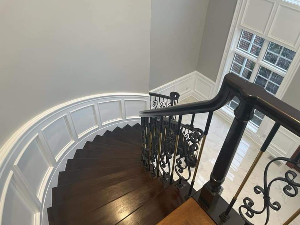 Dark wooden curved staircase with ornate iron railing, white trim, and a window.