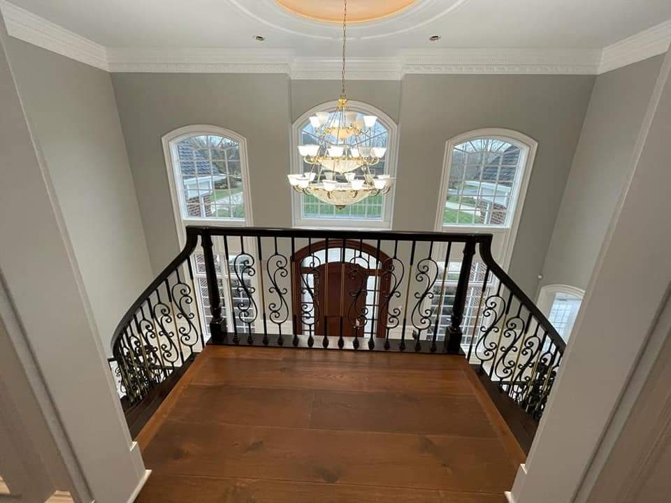 Looking down at a foyer with ornate railing, dark wood floor, chandelier, and arched windows.