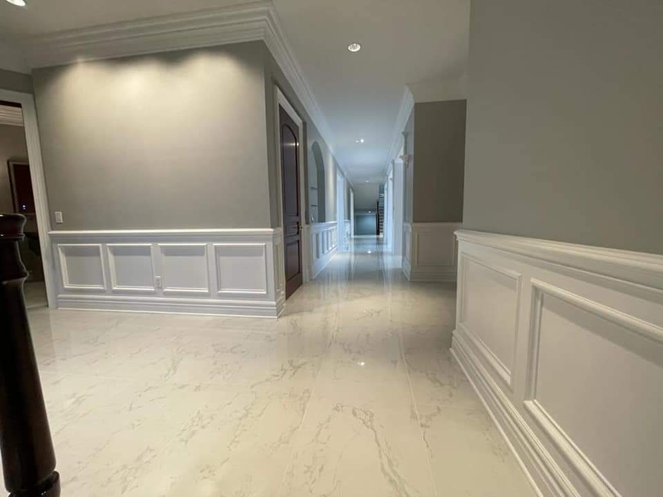 Long, bright hallway with white wainscoting, gray walls, and glossy marble flooring.