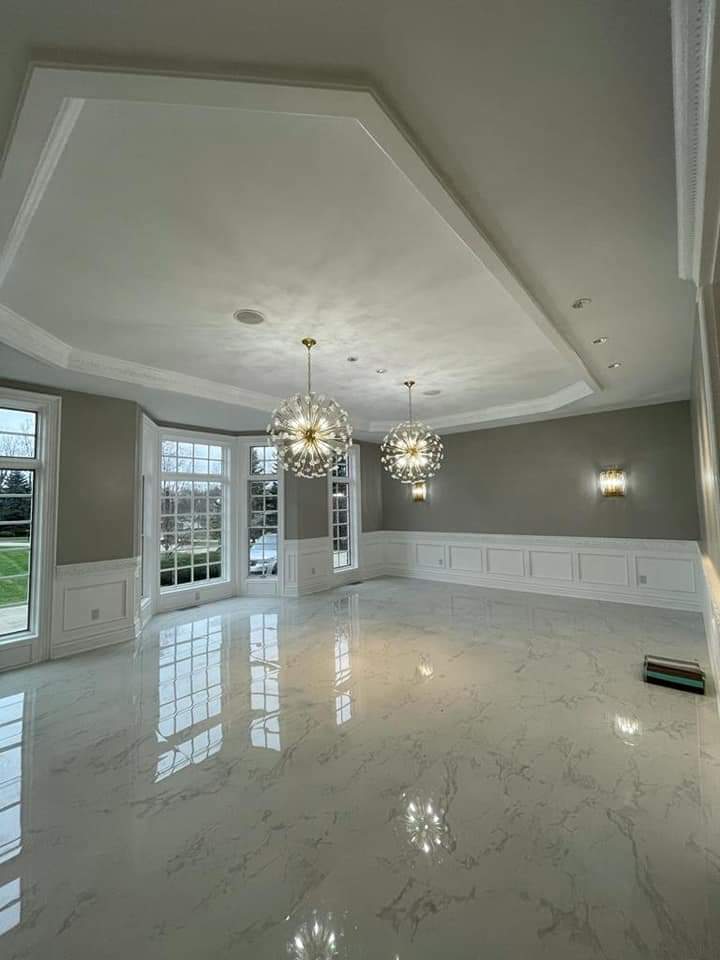 Empty, light-filled room with marble floors, chandeliers, and large windows. Walls are white and gray.