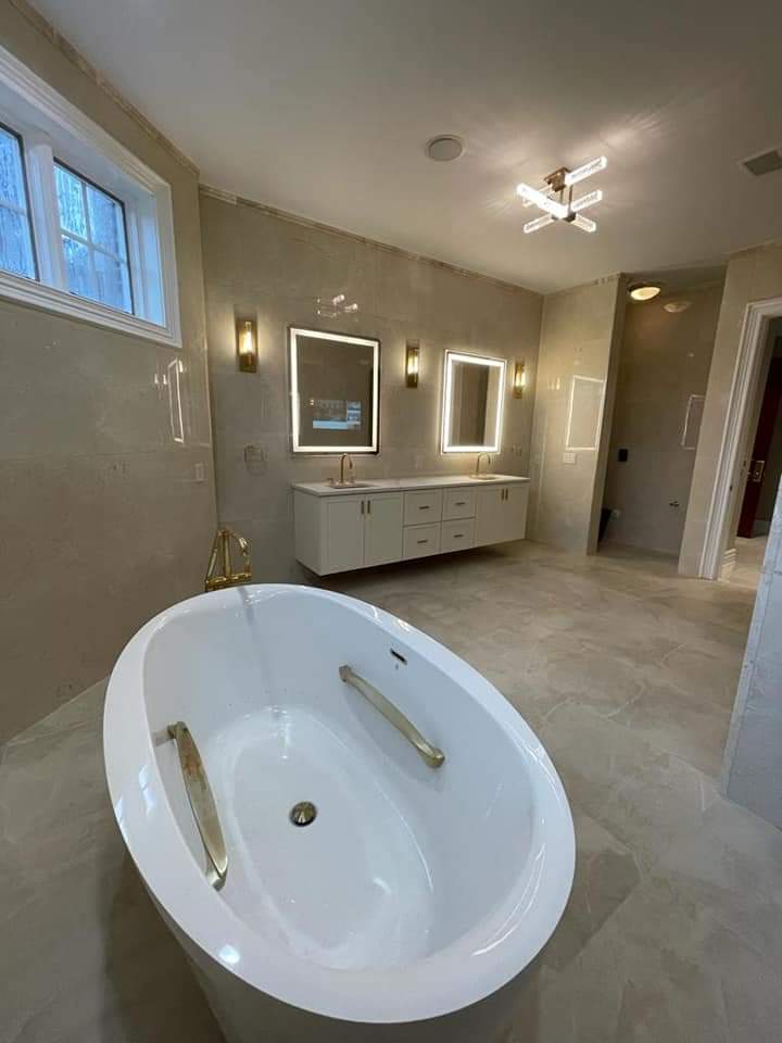 Modern bathroom with a white oval bathtub, double vanity with lighted mirrors, and neutral walls.