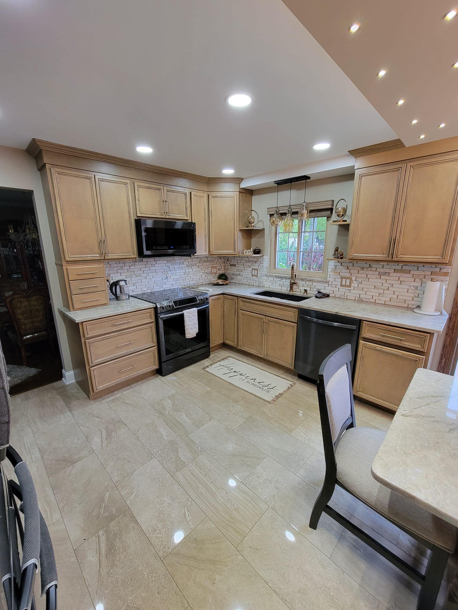 Kitchen with light wood cabinets, black appliances, and marble countertops.