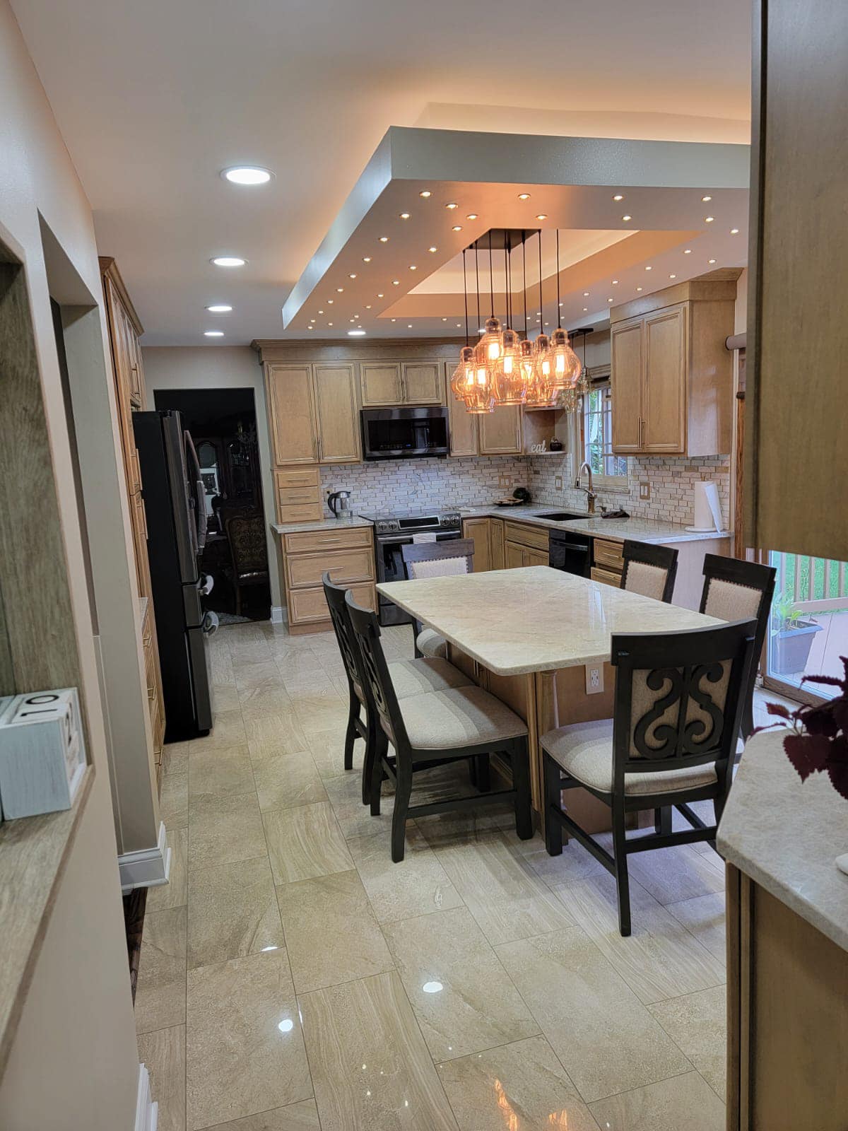 Kitchen with light wood cabinets, marble island with seating, pendant lights, recessed lighting.