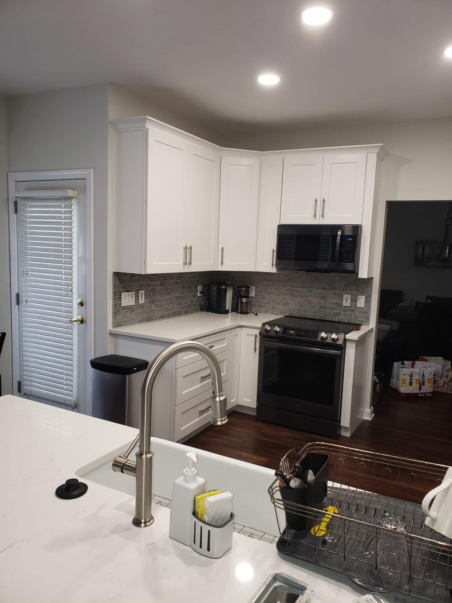 White kitchen with cabinets, stainless steel sink, black appliances, and dark wood floors.