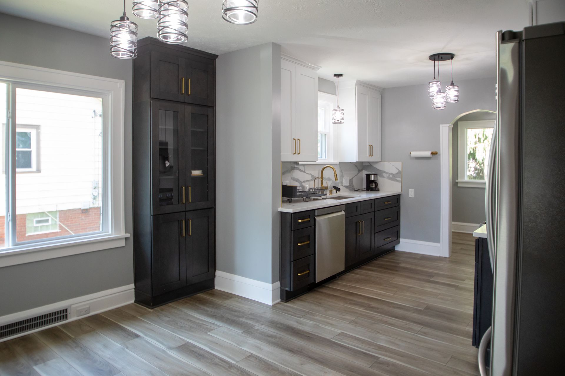 Modern kitchen with white and black cabinets, marble backsplash, hardwood floors, and overhead lighting.