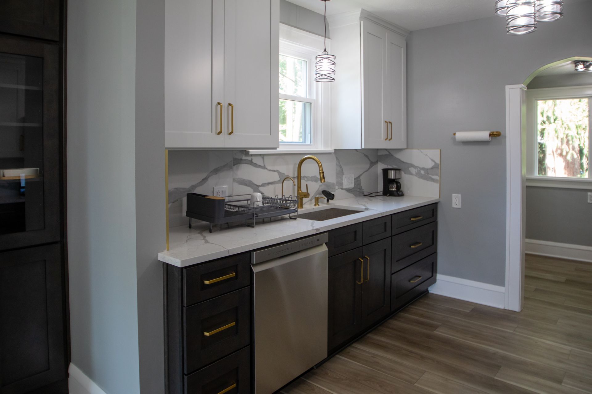 Modern kitchen with white and dark cabinets, marble backsplash, stainless steel appliances, and gold hardware.
