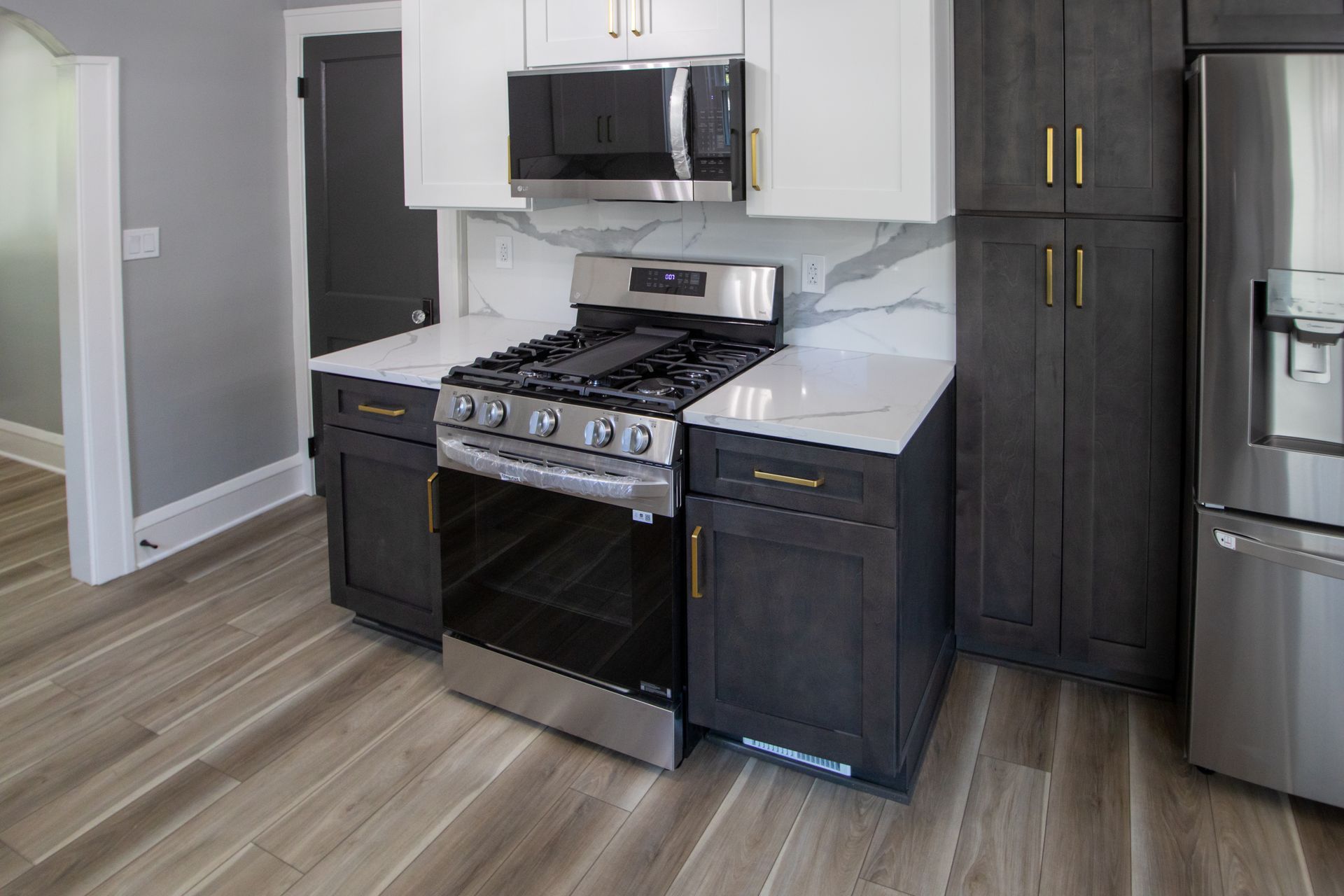 Modern kitchen with gray and white cabinets, stainless steel appliances, and wood-look flooring.