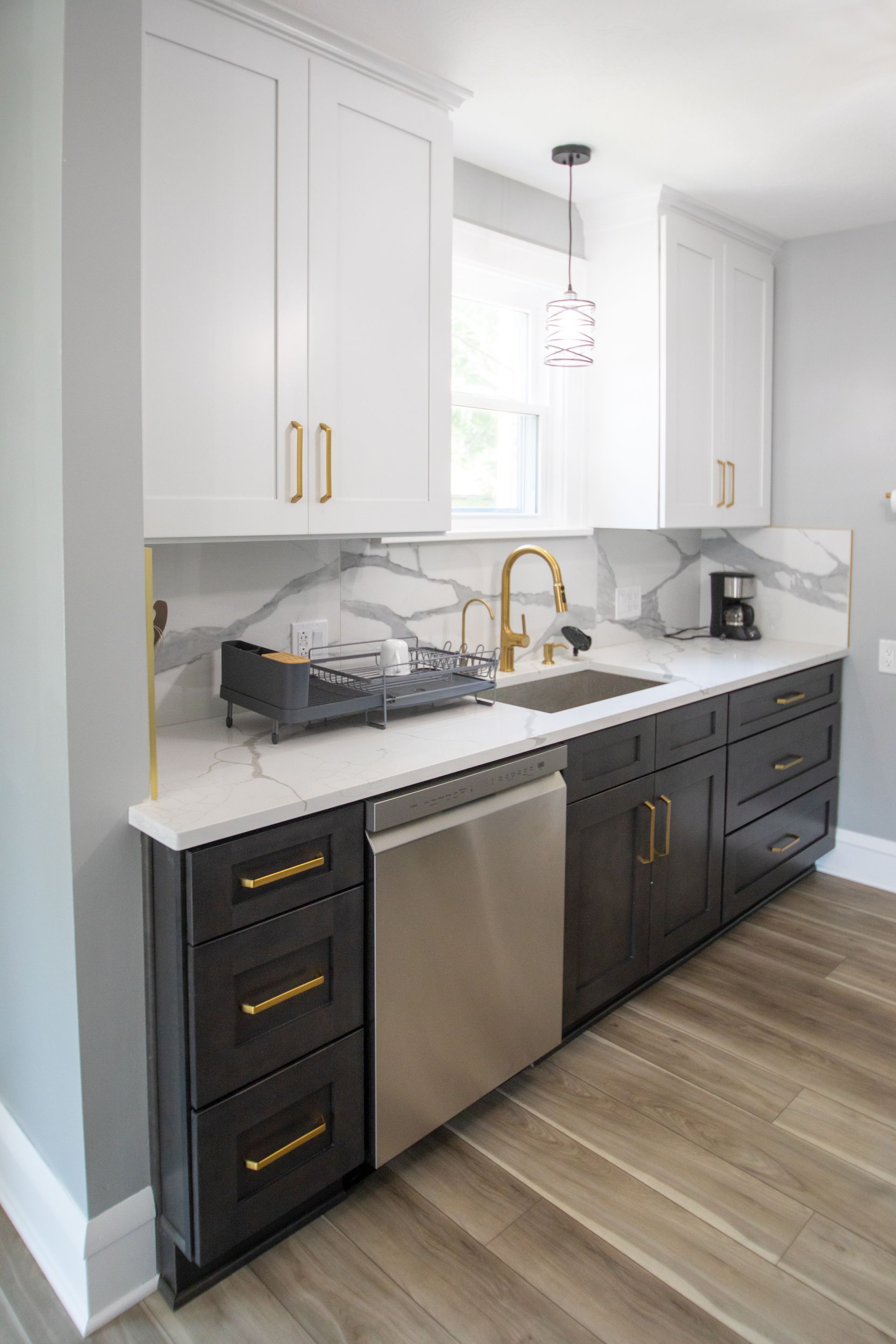 Modern kitchen with white and dark gray cabinets, stainless steel appliances, gold hardware, marble backsplash.