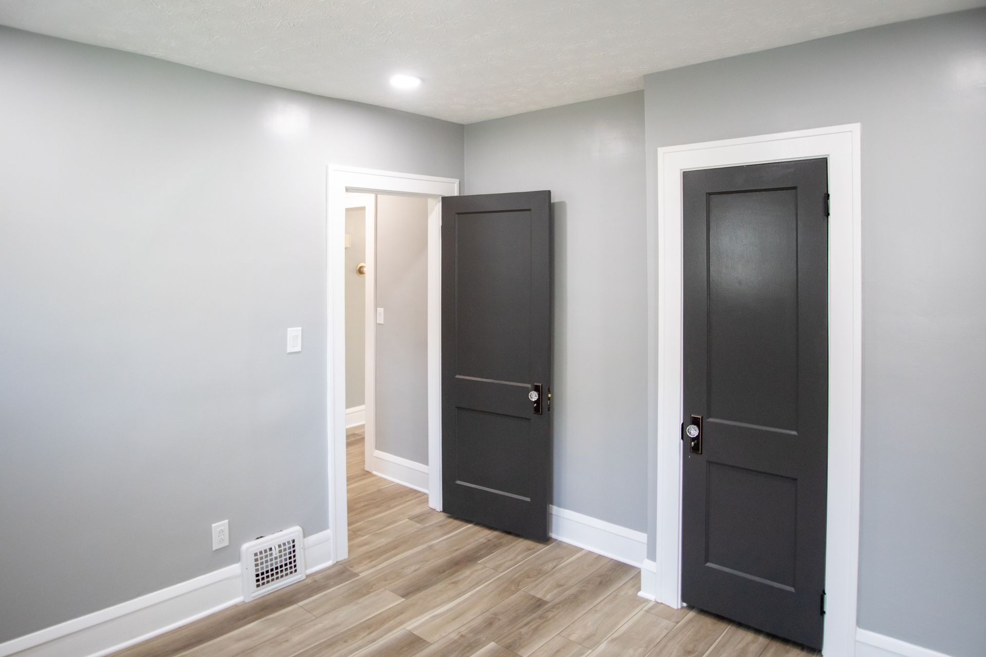 Empty room with gray walls, dark doors, white trim, and wood-look flooring.