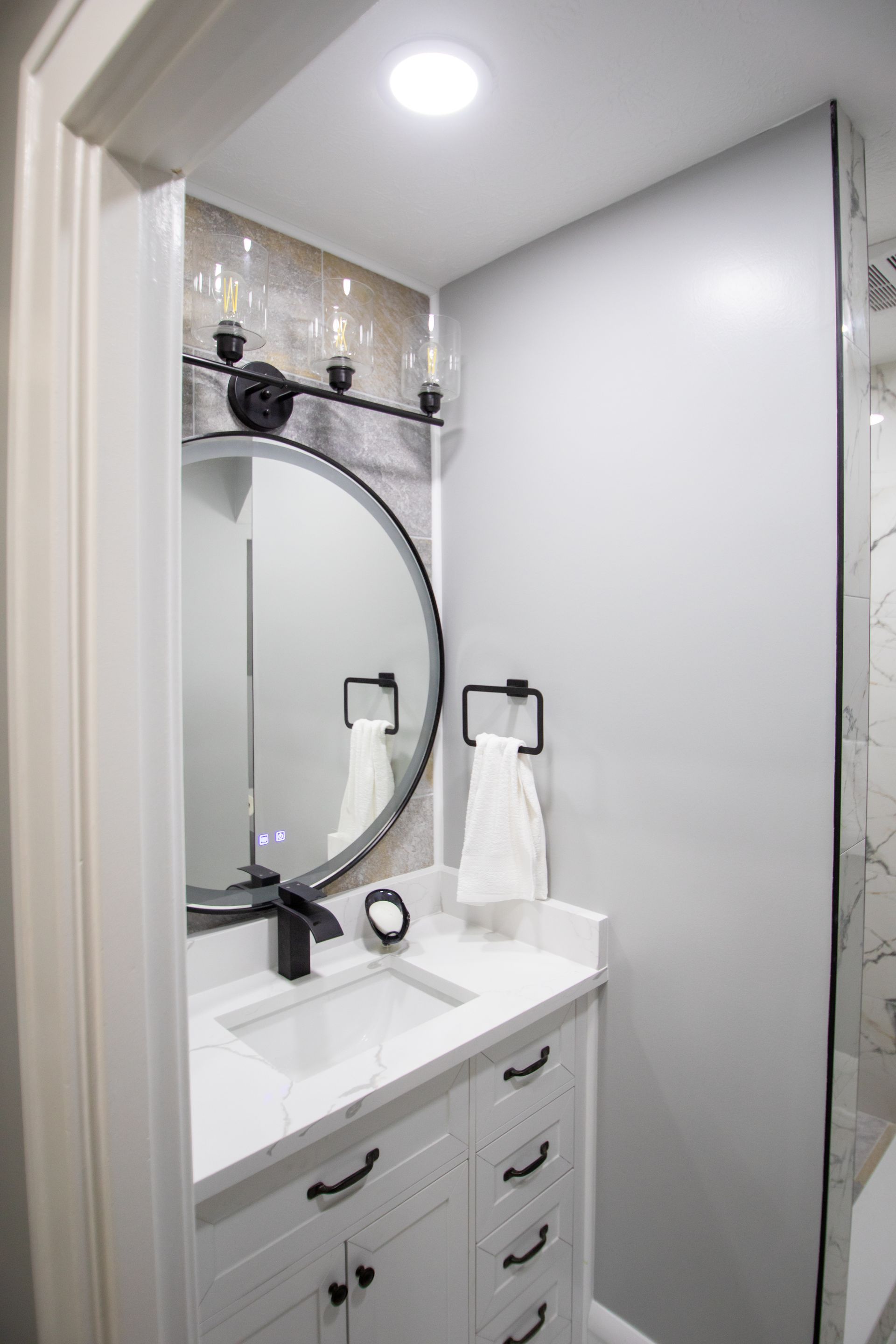 Modern bathroom with a round mirror, black fixtures, and white vanity.